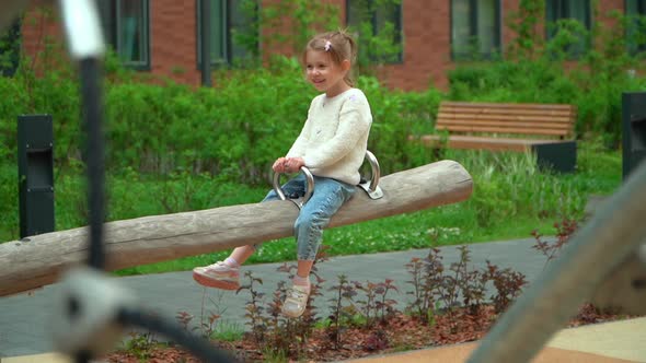 Happy Little Girl Swing on Swing on Playground Outdoors in Green Summer Park
