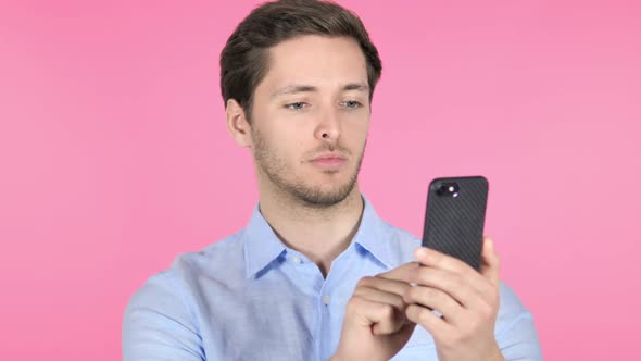 Young Man Using Smartphone on Pink Background alt