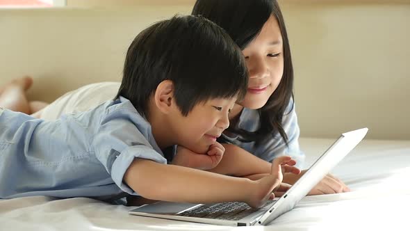Cute Asian Children  Lying In Bed And Using Laptop On White Bed alt