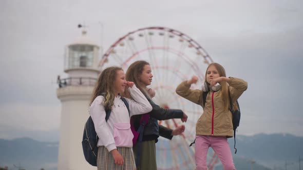Three Laughing School Girl Friends Jump in Dance and Fool Around Near Luna Park alt