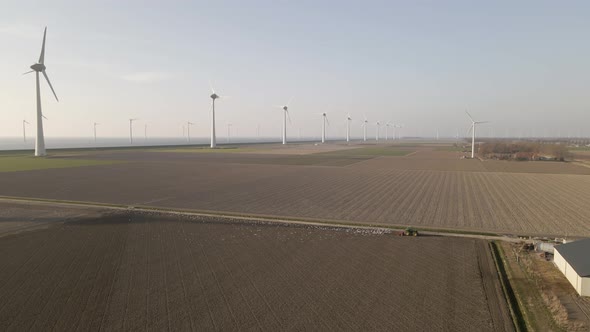 Aerial rural scene, Birds follow tractor plowing on endless field with wind turbines Landscape alt