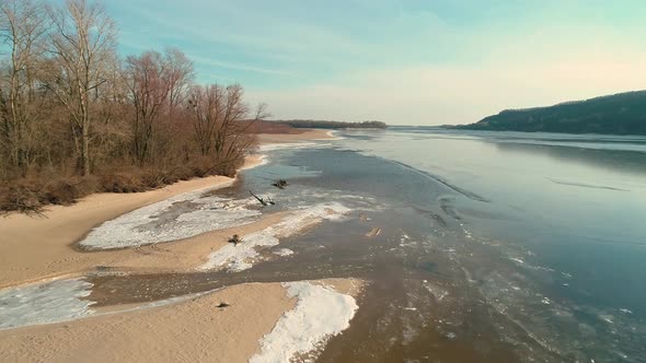 Aerial Drone Footage of Flight Over a Sandy Shore with a Small River in Winter alt