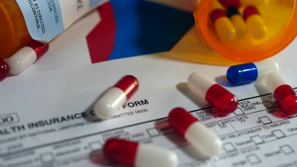 Cancer drug pills falling on a prop medical insurance form showing high cost of chemotherapy treatme alt