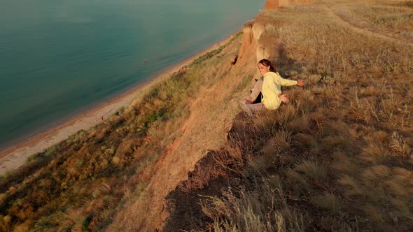 Happy Carefree Woman with Dog Sitting on Cliff and Enjoying Amazing View Above Sea Water alt