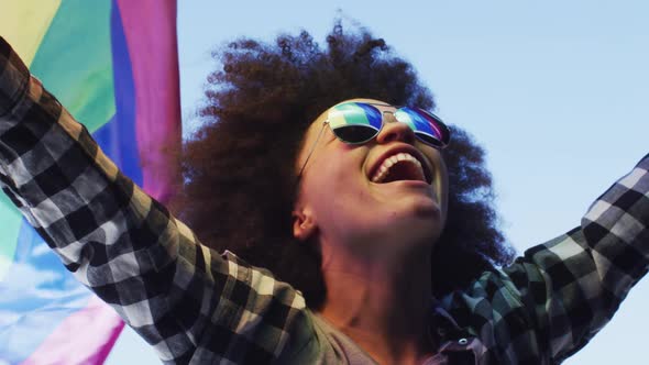 African american woman wearing sunglasses holding lbgt flag up in the air alt