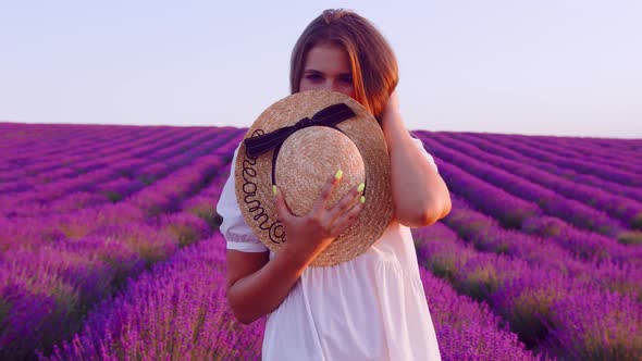 Beautiful Young Woman Wearing White Dress and Hat Standing in a Lavender Field