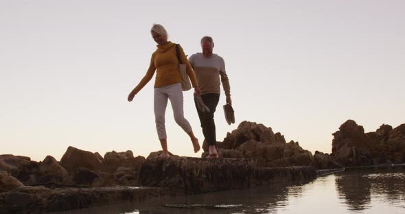 Senior couple walking while holding hands at beach alt
