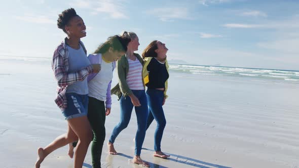 Happy group of diverse female friends having fun, walking along beach alt