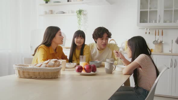Happy Asian Family Sitting Together at Kitchen Table and Talking Little Girl Telling Story to Mom alt