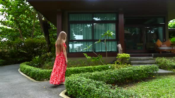 Traveller Woman in Red Dress Walking Barefoot on Path in Modern Tropical Resort alt