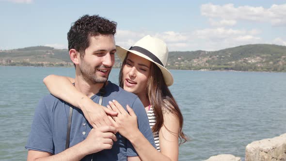 Smiling woman embracing boyfriend at lake in summer alt