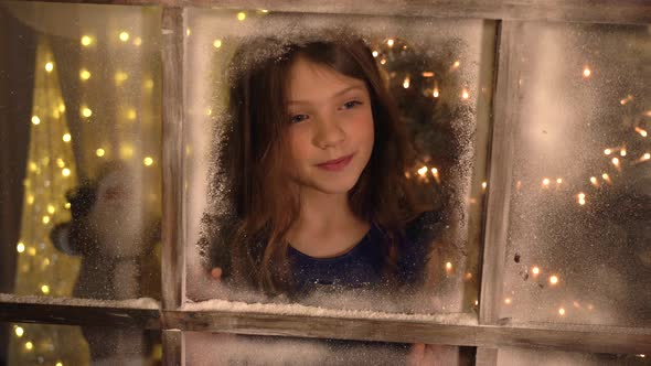 Stunning creative Christmas Holiday scene with pretty girl looking through window - slow motion