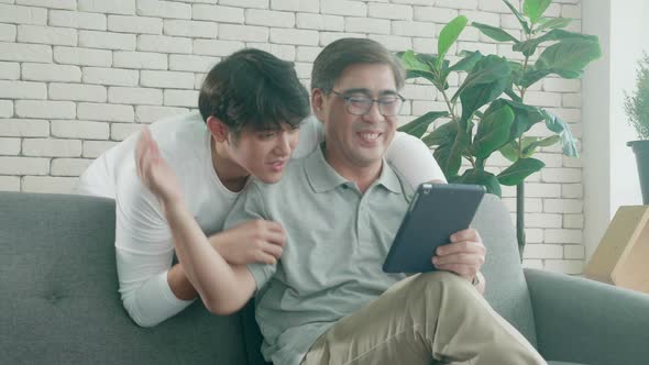 Happy family with father and son sitting on sofa and discussion with interesting on tablet computer.