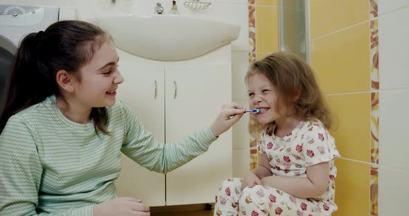Little Two Sisters Brushing Their Teeth Each Other Intensely in the Bathroom alt