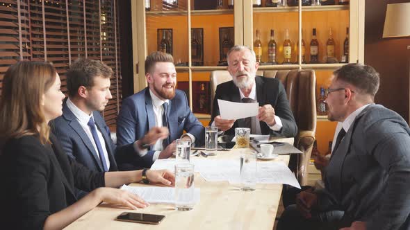 Gray Haired General Director Examining Terms of Transaction Against the Wall with Collection of