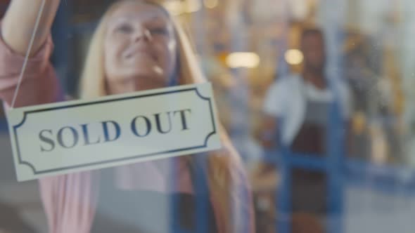 Cheerful Senior Female Bakery Owner Hanging Sold Out Sign on Glass Door alt