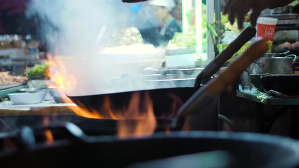 Asian Street Food: Man Frying Vegetables in Wok at Night Food Market in Chinatown. Slowmotion