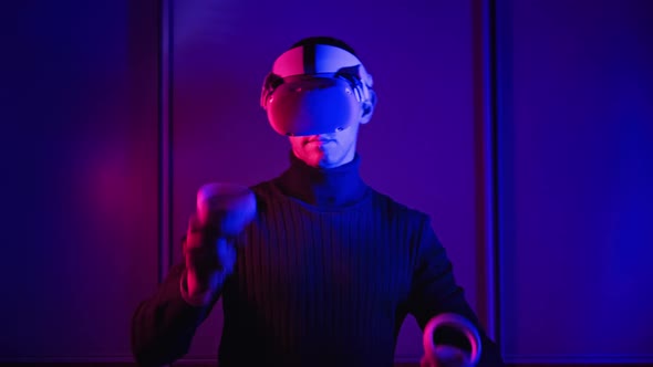Young Man in VR Helmet Interacts with Virtual Reality Using Controllers alt