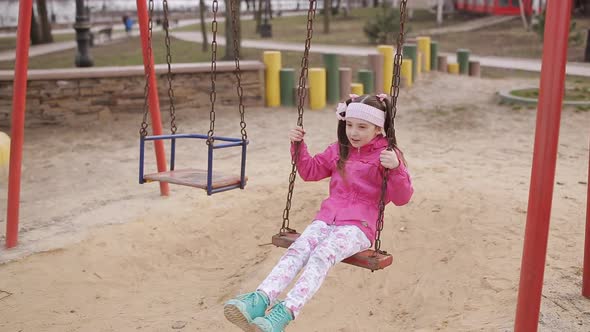 Little Girl Rides a Swing in the Park on the Playground