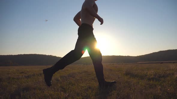 Young Muscular Man Running Through Field with Beautiful Landscape at Background alt