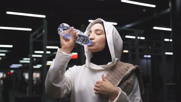 Portrait of a Muslim Woman in a Sports Hijab Who Drinks Water After a Workout alt