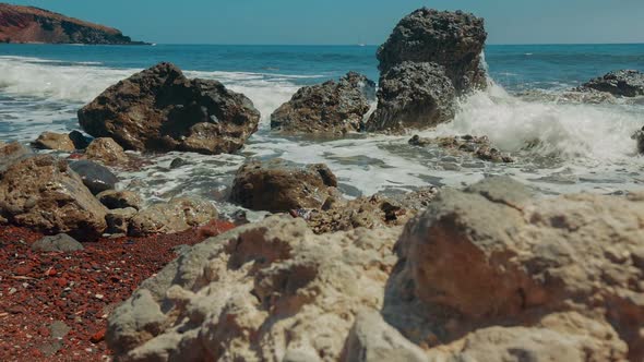 Slider Shot of Mediterranean Volcanic Beach with Red Sand and Surf Hitting the Rocks alt