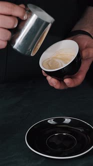 Barista pouring milk in hot coffee and making cappuccino foam in cafe close up, vertical alt