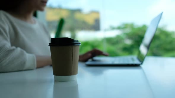 Closeup of a woman drinking coffee while working and typing on laptop computer keyboard