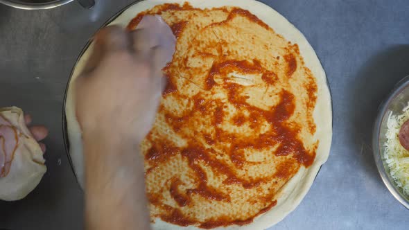 Male Hand Putting Slices of Sausage on the Pastry in Metal Form at Wooden Surface alt