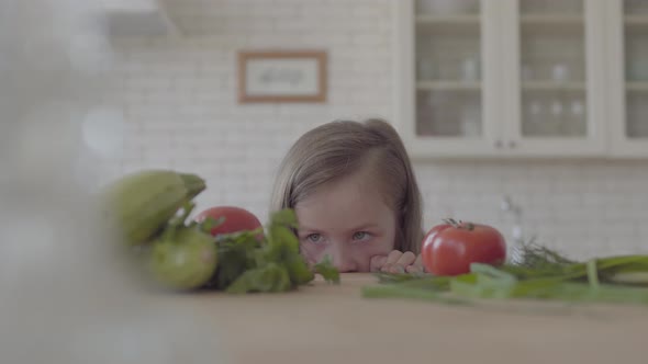 Small Girl Looking at the Table with Tomatoes Zucchini Greens Onion alt