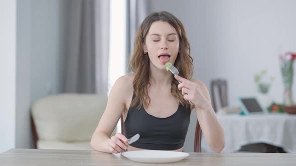 Front View Portrait of Slim Charming Young Caucasian Woman Cutting Cucumber Slice Eating Healthful alt
