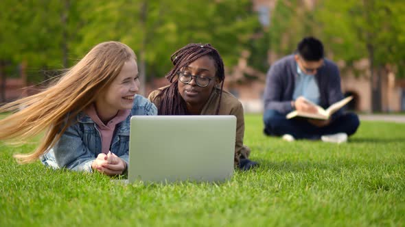 Diverse Friends Students Lying Outdoors on Lawn with Laptop Chatting and Smiling alt