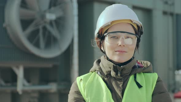 Portrait of a Woman Power Engineer in a Helmet on the Background of a Transformer.
