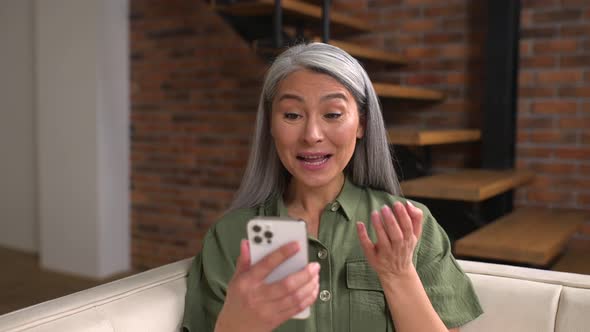 Smiling Asian Lady Waving Hello Greeting Friend or Family Using Mobile App for Video Calling