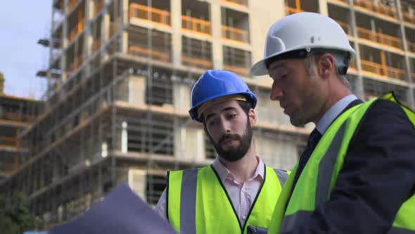 Male architect discussing with blueprint at construction site