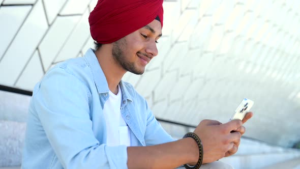 Portrait of Cheerful Young Indian Guy in Turban Sending Message on Mobile Phone