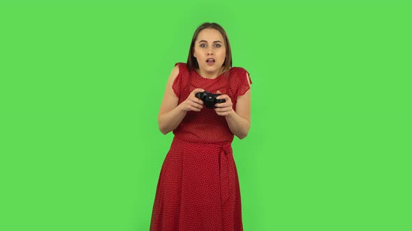 Tender Girl in Red Dress Is Playing a Video Game Using a Wireless Controller and Rejoicing in alt