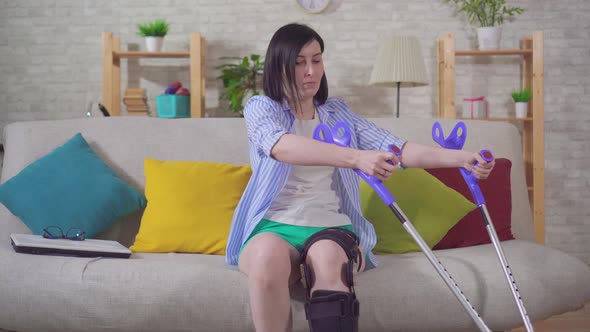 a Young Woman After Injury Knee Bend Orthosis Knee Brace Using Crutches Gets Up From the Sofa alt