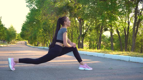 Young Athletic Woman in Black Sportswear Does Stretching Exercises Outdoor.