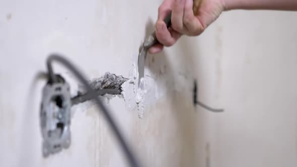 Builder with Putty Closes Cracks in Concrete Wall After Laying Electrical Wiring alt