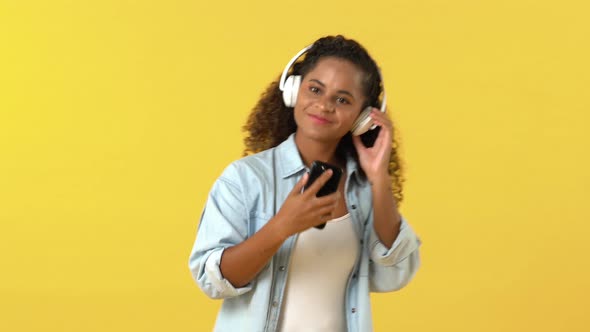 Happy African American woman wearing headphones moving body while listening to music