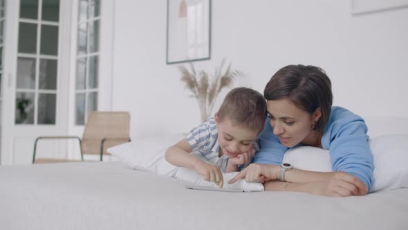 Mother and Son Using Digital Tablet in Bedroom at Home alt