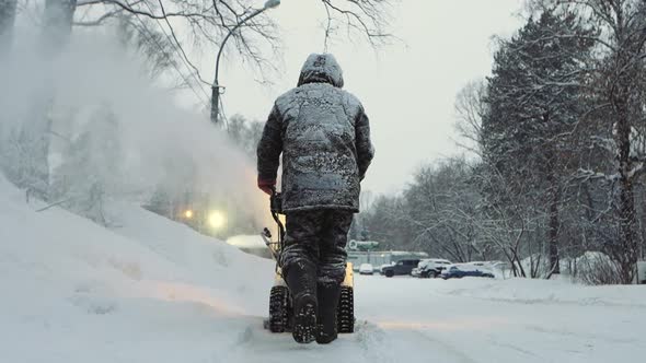 Snowcovered Man Cleans the Road in Winter with Blower Snow Removal Equipment alt