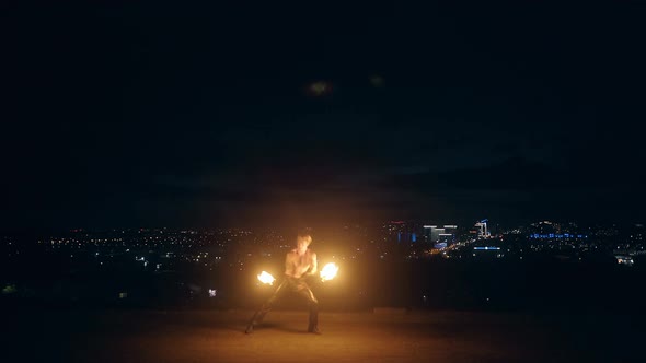 Young Blond Male Does Fire Dance with Two Torches Spins Torches in the Middle of the Night with City alt