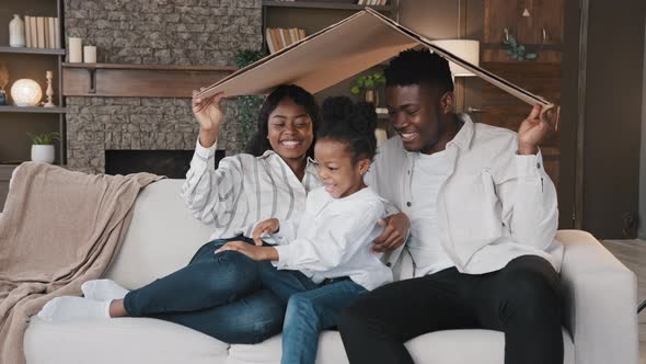 African Couple Sitting on Couch Under Cardboard Roof Smiling Looking at Camera Active Happy Daughter alt