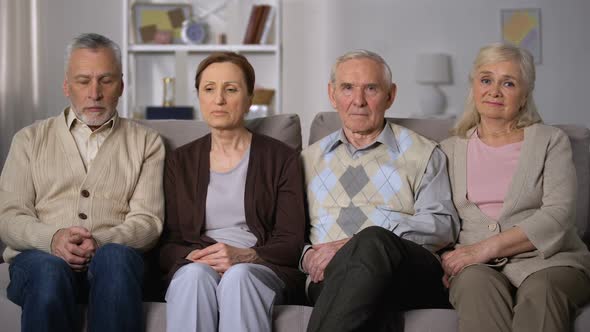 Upset Senior Friends Sitting on Sofa and Looking at Camera, Social Problems alt