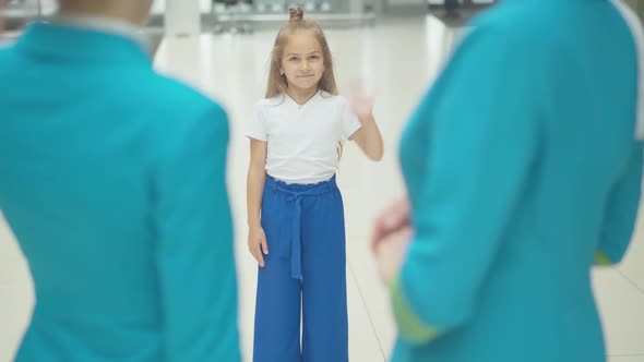 Portrait of Cute Little Caucasian Girl Waving To Unrecognizable Stewardesses in Airport. Pretty alt