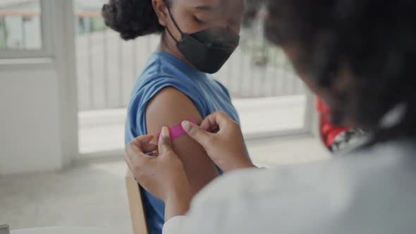 A female doctor is applying plaster to a child's shoulder after being vaccinated. alt