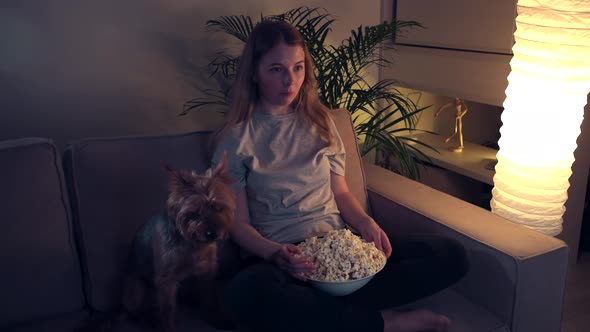 A Young Blonde Girl Is Watching TV with Her Beloved Little Dog. Friday Evening