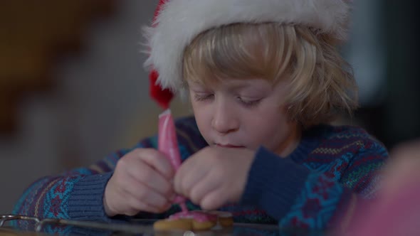 Closeup Focused Little Boy Decorating Gingerbread Cookie on Christmas Eve Indoors at Home alt